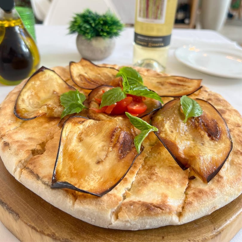 Focaccia topped with roasted eggplant, cherry tomatoes, and fresh basil, served on a wooden board.