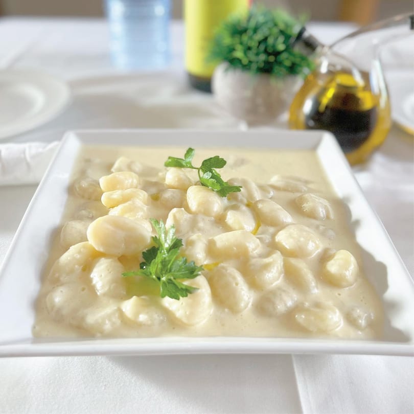 Creamy gnocchi pasta dish garnished with parsley on a white tablecloth with olive oil.