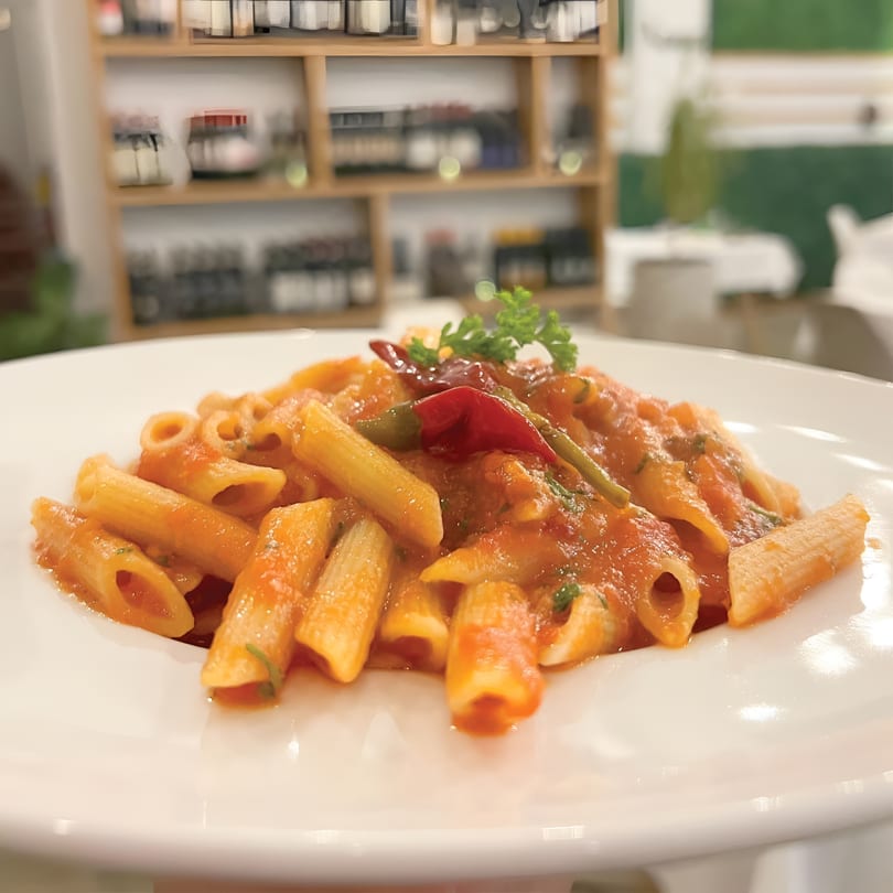 Penne pasta in a rich tomato sauce, garnished with fresh parsley and red chili peppers.